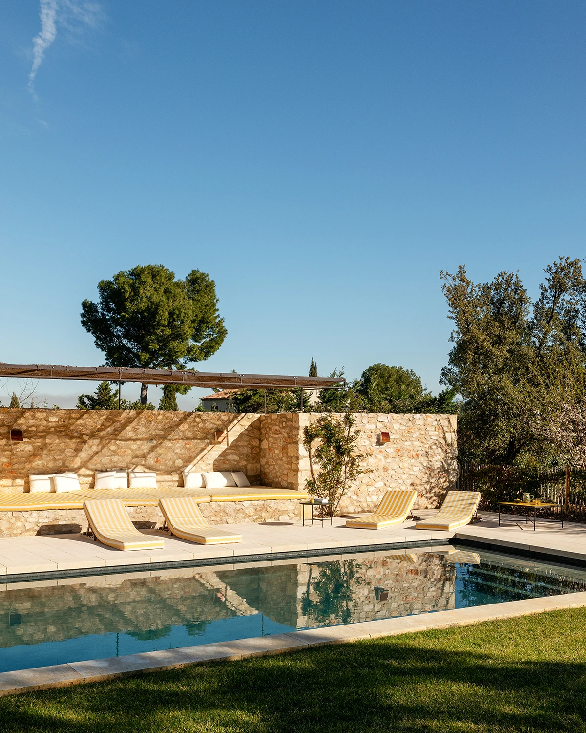 Skriveni draguljIza borova se skriva dugi betonskibazen u boji lagune. Ležaljke pomjeri (Beach Concept). Nakamenom zidu zidna svjetiljka(Honoré). Niski stolići od zelligespločica (Art & Sud).